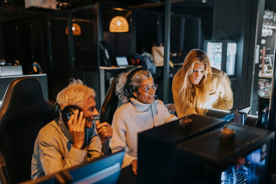Woman helping senior couple playing computer game at gaming lounge during weekend