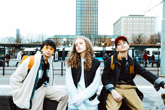 Portrait of multiracial male and female friends sitting on bench in city during weekend