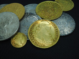 Spanish Escudo and Real coins in gold and silver on a black background - obrazy, fototapety, plakaty