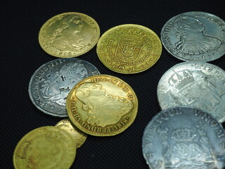 Spanish Escudo and Real coins in gold and silver on a black background - obrazy, fototapety, plakaty