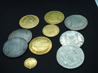 Spanish Escudo and Real coins in gold and silver on a black background