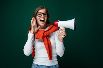 Young woman with brown hair dressed in a white turtleneck holds a loudspeaker, news and advertising...