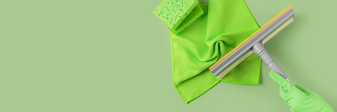 Set For Cleaning Windows And Other Surfaces On Green Background. Hand In Rubber Glove With Mop. Cleaning Concept, Professional Cleaning, Household Supplies. Top View, Long Banner With Copy Space