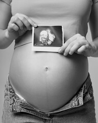 Black and white photo of Pregnant female is holding sonogram baby embryo image over a pregnant...