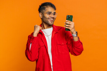 Happy excited Indian Hindu man guy use smartphone typing browsing shouting say wow yes found out great big win good news lottery goal achievement celebrating success, winning play game on orange