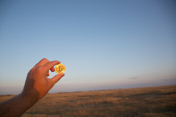 Bitcoin coin in hand at sunset