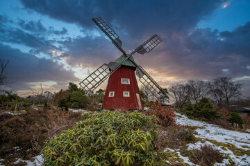 Typical historical red wooden windmill in a winter landscape. Sunset on the coast on a rock. Stenungsund in Sweden
