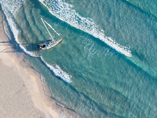 Aerial view of a stranded sailboat on a white sand beach shore with turquoise water color