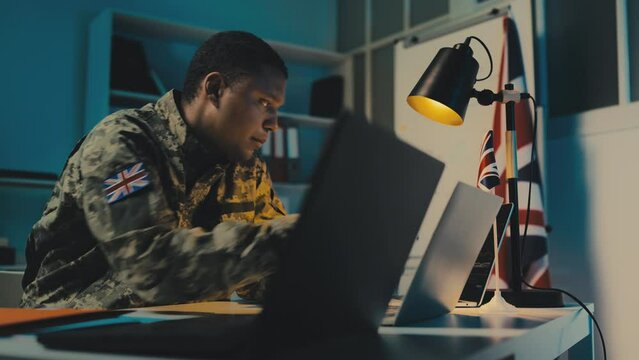 British army officer typing on laptop in office, planning mission strategy