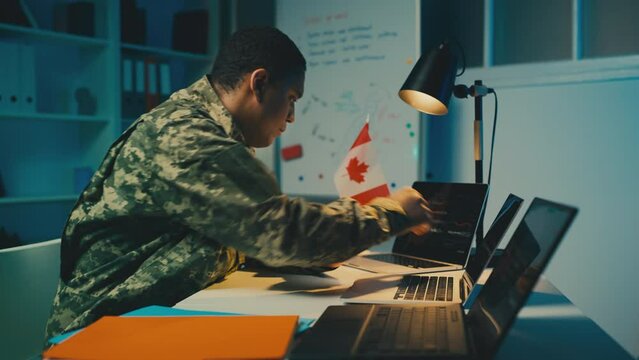 Canadian military officer working in office, planning operations on laptop