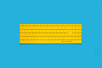 Yellow wireless keyboard on blue background. Top view, flat lay