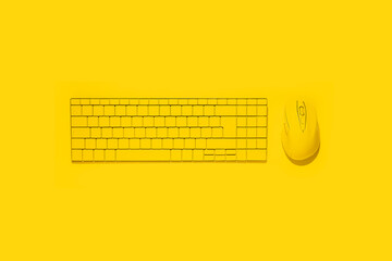 Yellow keyboard and yellow computer mouse on a yellow background. Top view, flat lay