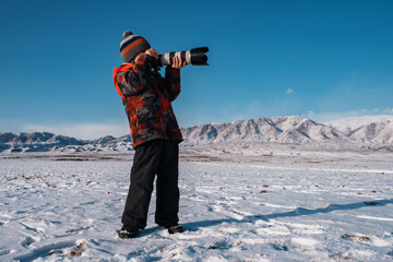 Boy with professional camera on mountain background in winter