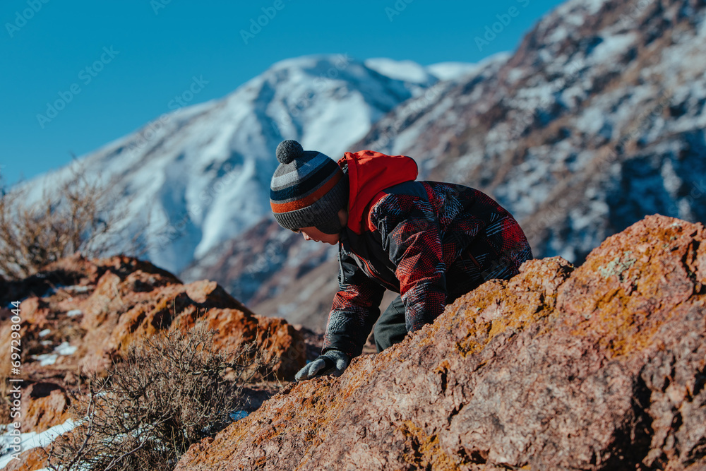 Sticker Boy climbing on big boulder in the mountains in winter