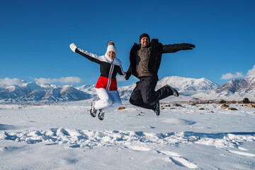 Happy young couple jumping on mountains background in winter season