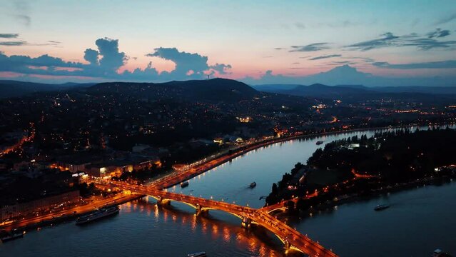 Aerial drone night dolly shot of river cruise ships, bridges illuminated after sunset in Budapest, Hungary