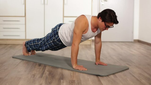 a young guy with glasses was doing push-ups at home on a mat, not in sportswear