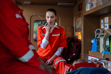 rescue nurse holds a walkie-talkie wearing a uniform and rushes to help a patient who has been in an accident. The team helps CPR the injured person and uses a life support machine in the ambulance. - obrazy, fototapety, plakaty