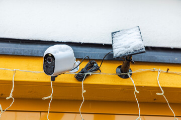 Close-up view of outdoor surveillance with a snow-covered solar panel on facade of villa on frosty...