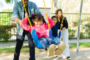 Happy children playing on the swings with their parents