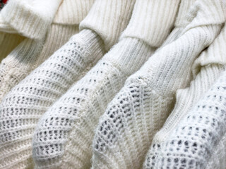 Row of light white color Knitted sweaters hanging on hangers for sale.