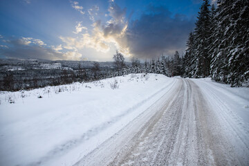 Winter landscape in the sunset. A road full of snow leads through a forest with snow-covered pine...
