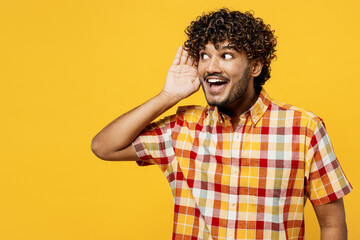 Young surprised shocked curious nosy Indian man he wears shirt casual clothes try to hear you overhear listening intently isolated on plain yellow color background studio portrait. Lifestyle concept.