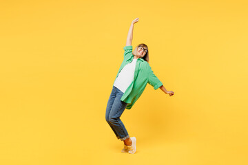 Full body elderly blonde woman 50s year old wear green shirt glasses casual clothes lean back stand on toes with outstretched hands dance isolated on plain yellow background studio. Lifestyle concept - obrazy, fototapety, plakaty
