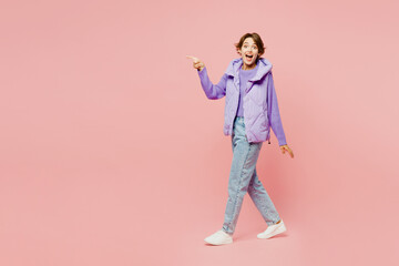 Full body side view surprised young woman wears purple vest sweatshirt casual clothes point index finger aside on area walking going isolated on plain pastel light pink background. Lifestyle concept.