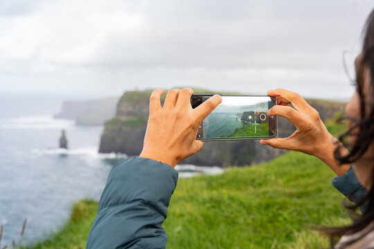 close up of hands with mobile phone taking horizontal photograph of a beautiful seaview with blurred cliffs in the background