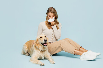 Full body young sick ill sad owner woman wear casual clothes sit near her best friend retriever dog blow nose using napkin isolated on plain light blue background studio. Allergy health care concept.