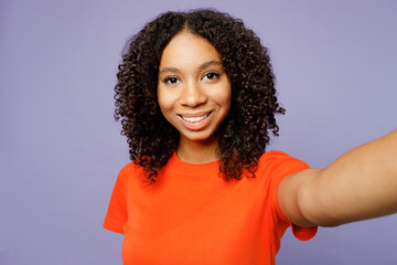 Close up little kid teen girl of African American ethnicity wear orange t-shirt doing selfie shot pov on mobile cell phone isolated on plain pastel light purple background Childhood lifestyle concept