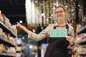 Young seller consultant woman wears uniform point on aisle hold card sign with open title text,...