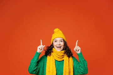 Young surprised woman she wear green knitted sweater yellow hat scarf pointing index finger...