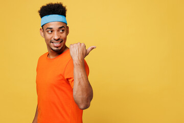 Young fitness trainer instructor sporty man sportsman in orange t-shirt point thumb finger aside on...