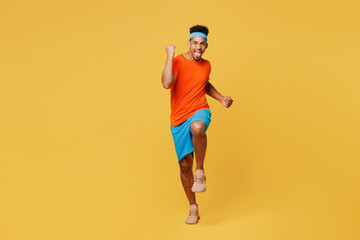 Fototapeta na wymiar Full body happy excited young fitness trainer sporty man sportsman wear orange t-shirt doing winner gesture spend time in home gym isolated on plain yellow background. Workout sport fit abs concept.