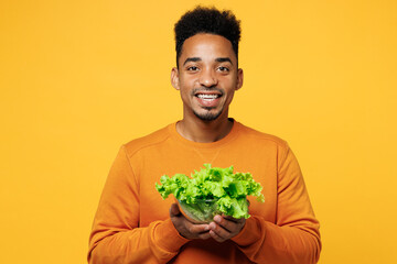 Young man in orange sweatshirt casual clothes hold bunch of fresh greens lettuce leaves in bowl...