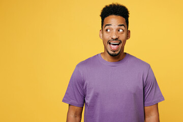 Young surprised shocked happy fun man of African American ethnicity he wearing purple t-shirt casual clothes look aside on area isolated on plain yellow background studio portrait. Lifestyle concept.