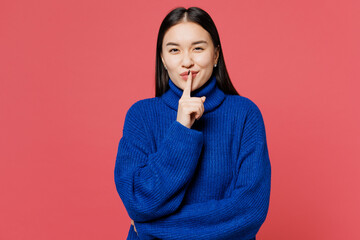 Young secret woman of Asian ethnicity wear blue sweater casual clothes say hush be quiet with finger on lips shhh gesture isolated on plain pastel pink background studio portrait. Lifestyle concept.