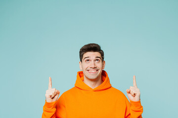 Young smiling happy fun man he wear orange hoody casual clothes point index finger overhead on area...