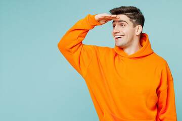 Young smiling happy man he wears orange hoody casual clothes hold hand at forehead look far away...