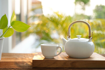 white tea cup and tea pot and plant pot and notebook on wooden tray and table balcony outdoor view