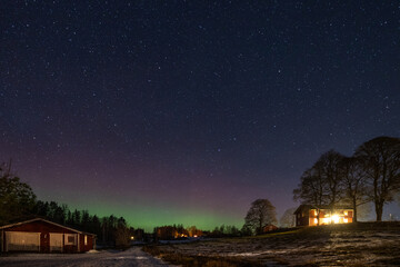 Winter landscape with wooden house under a beautiful starry sky and Northern Lights