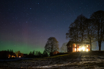 Winter landscape with wooden house under a beautiful starry sky and Northern Lights