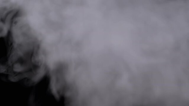 Plumes of Thick Icy Clouds of Smoke or Steam Fill the Space in Blurry Motion. Swirl of soft white curls of clouds of smoke from vape, cigarettes dissolve on a black background. Texture. Full frame.