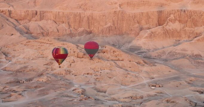Hot air balloon flying over 
 Hatshepsut Temple at sunrise in Valley of the Kings and red cliffs western bank of Nile river- Luxor- Egypt