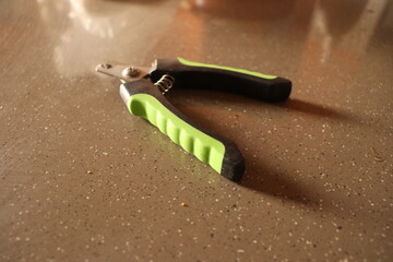 A green and black colored Dog or puppy nail cutter or trimmer on a brown Marble floor, reflection