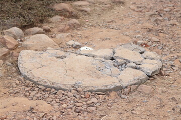 Old broken sewer hole cap made up of cement in a dirt ground