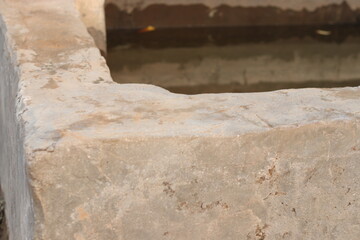 An old Traditional vintage stone or cement water well corner of cattle filled with water, square...