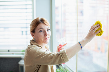 Focused woman cleaning the window glass inside her apartment